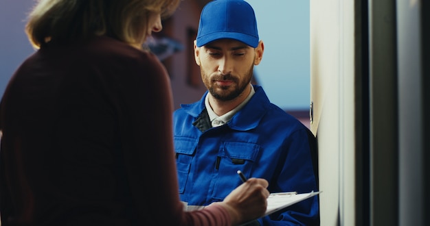 Back view on the Caucasian woman signing a clipboard when having a parcel delivery from mailman.