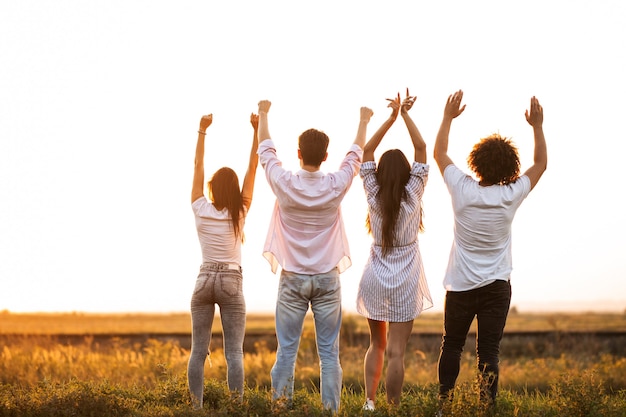 back view company of young girls and guys are standing in the field on a summer day