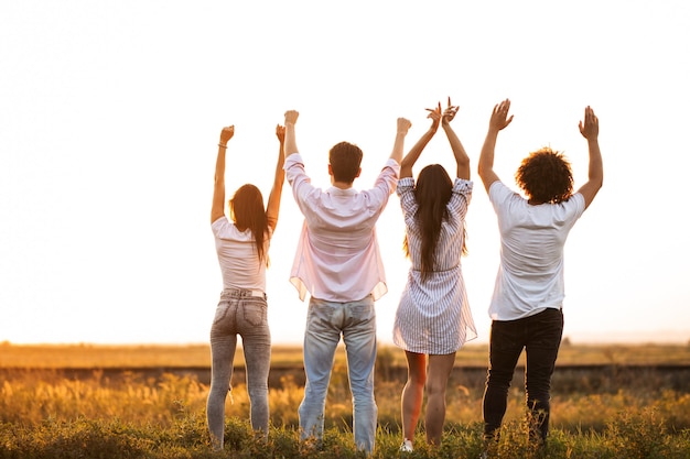 Back view Company of young girls and guys are standing in the field on a summer day