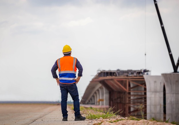 Vista posteriore del progetto di controllo dell'ingegnere edile presso il cantiere operaio caposquadra in elmetto protettivo presso il cantiere dell'infrastruttura