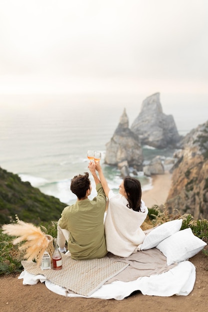 Back view of couple drinking champagne and clinking glasses enjoying ocean shore copy space vertical