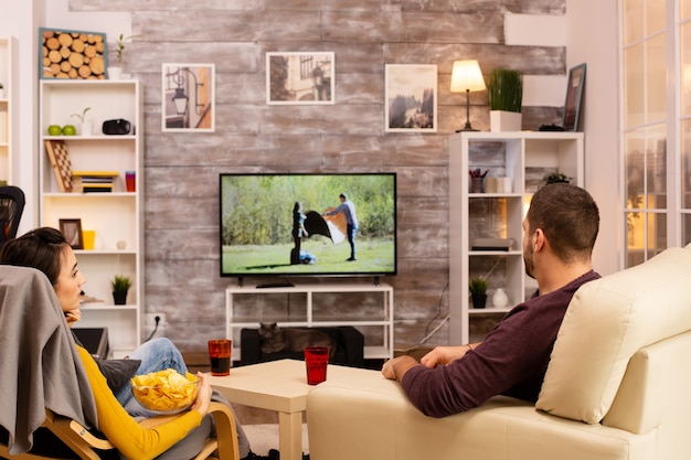 Vista posteriore di una coppia in soggiorno che guarda un film in tv mentre mangia cibo da asporto