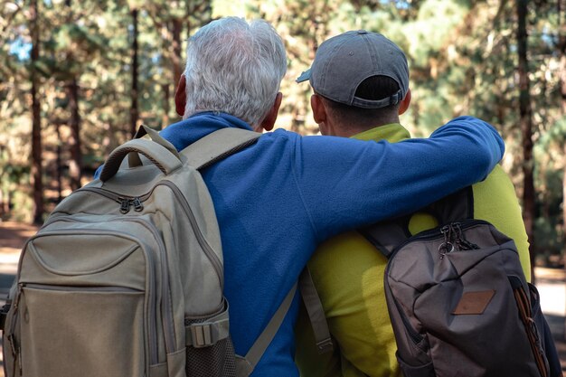 自然と健康的なライフスタイルへの同じ情熱を分かち合う森の中で一緒にハイキングをしている年配の祖父と若い孫のカップルの後ろ姿