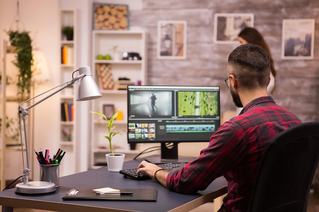 back view of creative filmmaker working on a movie on laptop. girlfriend in the background.