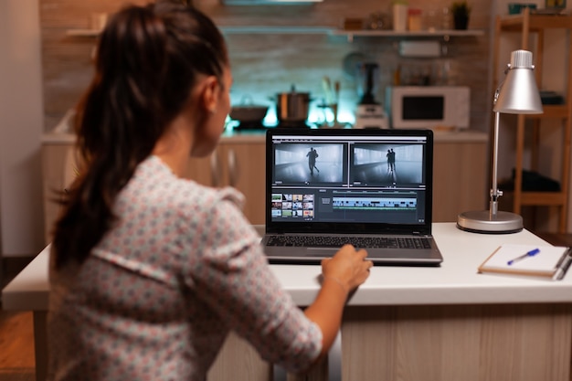 Back view of creative filmmaker working on a movie on laptop during midnight