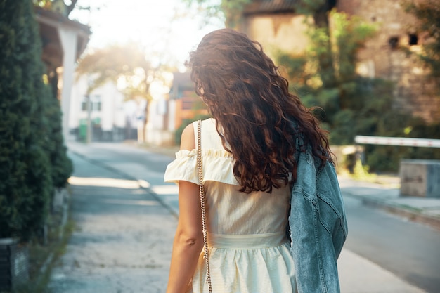 Back view curly woman walking on the city street