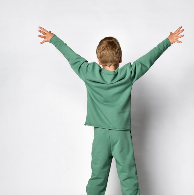 Вид сзади на симпатичного активного маленького мальчика в модной модной спортивной одежде, стоящего с широко раскинутыми поднятыми вверх руками, демонстрируя эмоции счастья и комфорта Позитивное веселое детское выражение