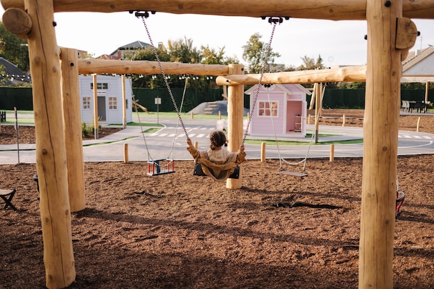 Back view of cute little girl swing on a swing in the specially designated place in the park softner