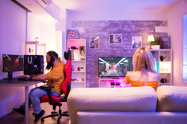 Back view of excited girl playing shooter games while sitting on sofa. colorful neon light. couple playing online games