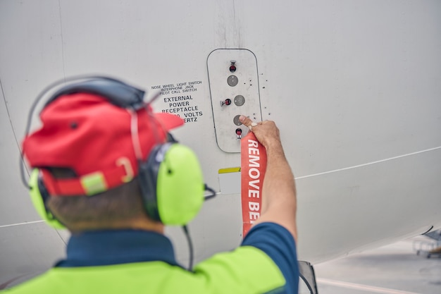 Foto vista posteriore di un tecnico esperto di manutenzione aeronautica maschio che apre la porta di accesso all'alimentazione esterna