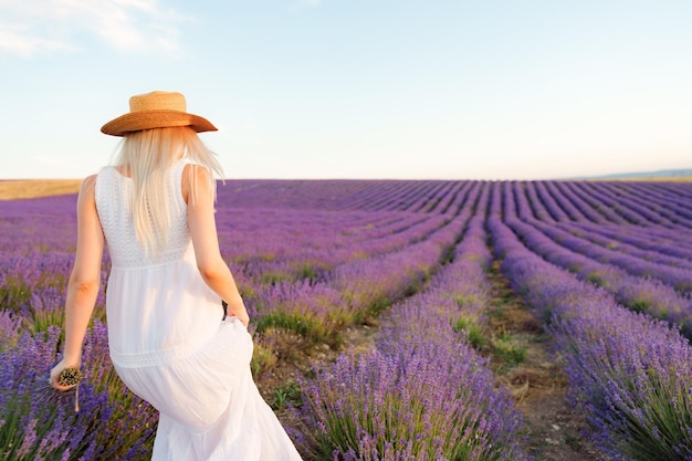 Вид сзади на женщину в платье и шляпе, стоящую на лавандовом поле