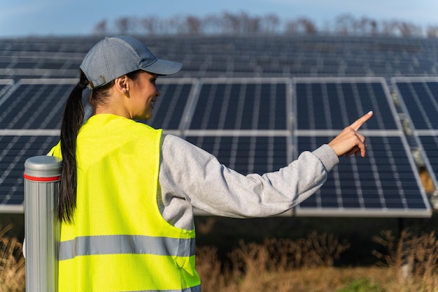 Back view of the female ecological engineer pointing away while collects efficient information about solar panels Photovoltaic solar farm green energy environment concept