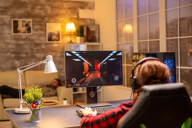 Vista posteriore del giocatore femminile che gioca su un potente computer pc a tarda notte nel soggiorno.