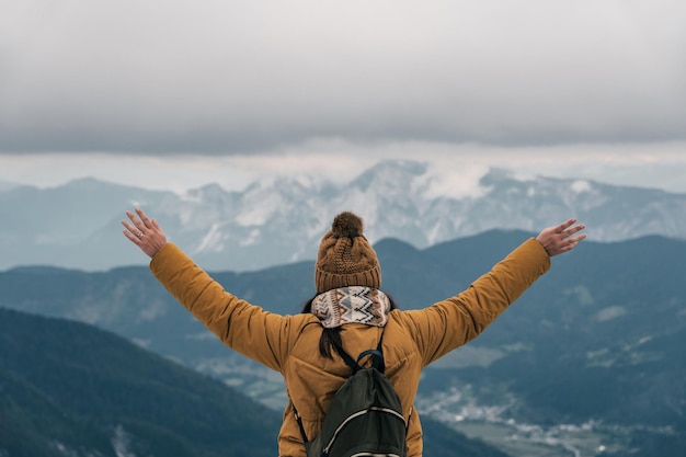 Photo back view of female hiker with outstretched arms looking at amazing view in mountains in winter