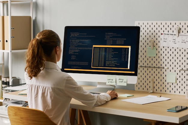 Foto vista posteriore programmatore femminile che scrive codice lavorando alla scrivania