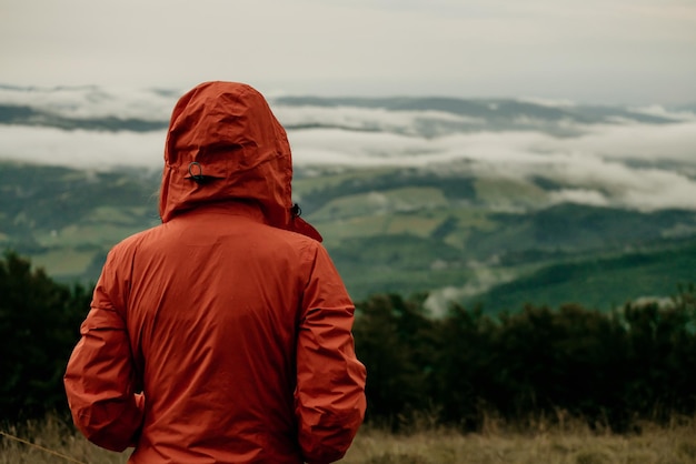 Back view of female tourist in orange jacket looking at beautiful scenery of mountains