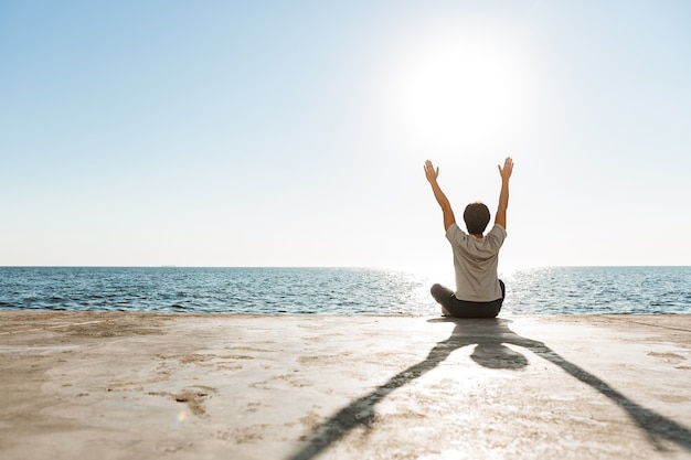 Back view of a fit asian man doing yoga exercises at the beach, meditating