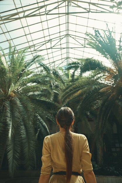 Vista posteriore misura la donna esotica che guarda le palme in un luccio tropicale