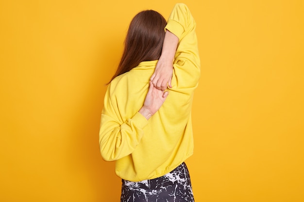 Photo back view of flexible attractive female clutches hands behind back in lock