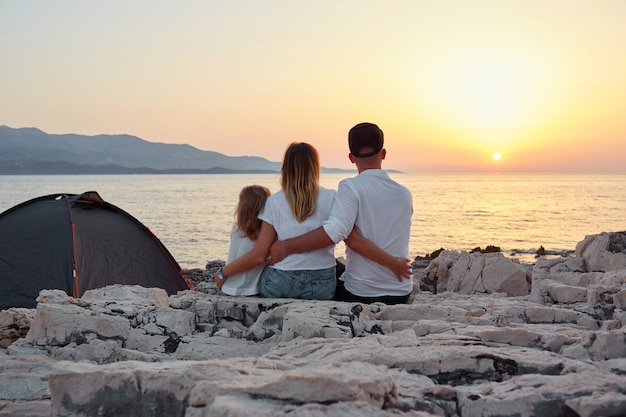 Photo back view of friendly family admiring setting sun over sea.