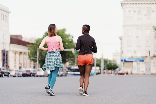 Вид сзади друзей в спортивной одежде, бегущих по городу, обсуждающих мультиэтнических женщин, занимающихся фитнесом