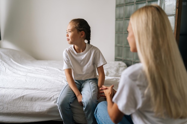 Back view from unrecognizable young mother talking counseling upset offended pretty child girl feels sad insulted sitting on bed at home