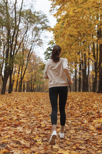 유산소 운동을 하는 동안 가을 공원에서 길을 따라 달리는 활동적인 여성 조깅하는 사람의 뒷모습 전신