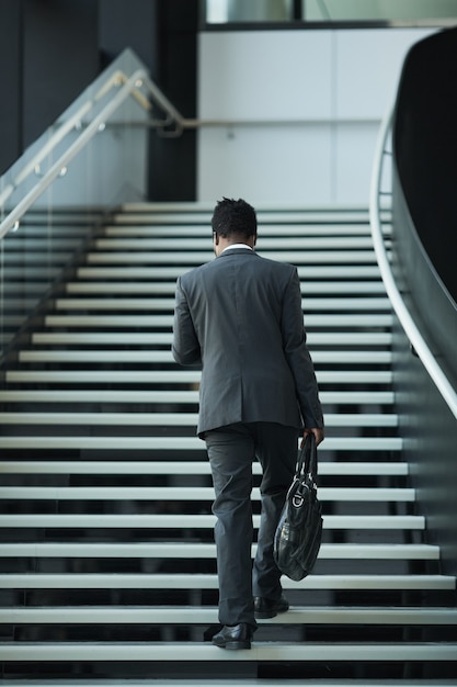 Back view full length at young African-American businessman walking up stairs in office building