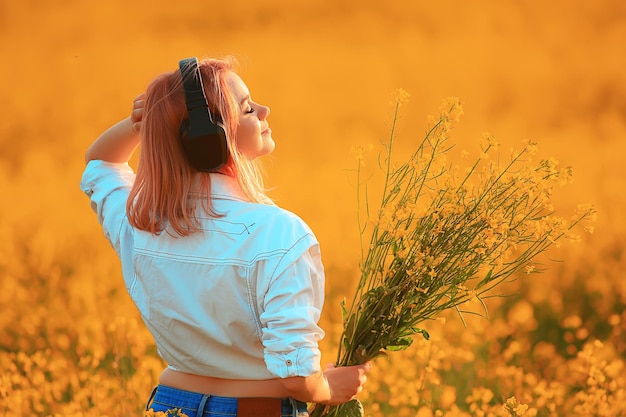 Vista posteriore di una ragazza in cuffia che ascolta la musica in un campo di fiori, la musica primaverile è felice