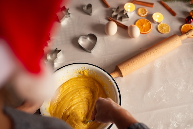 Photo back view of a girl in red santa hat making dough in the bowl