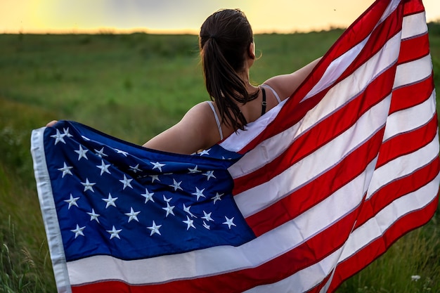 Back view of a girl with an American flag running on the grass in the field