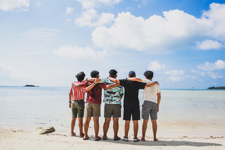 Photo back view of group of friends standing and embrace each other on tropical beach during vacation