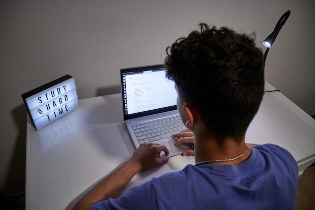 A back view of a guy studying with a sign quotstudy hard timequot on the desk