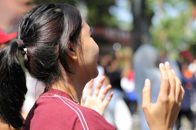 幸せなアジアの若い女性が夏祭りの音楽フェスティバルで群衆と踊っている後ろの景色