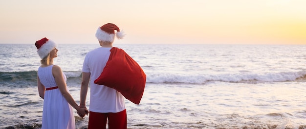 Back view Happy family in Santa Claus hats celebrating Christmas on beach people traveling to warm countries on winter tour New Year and Christmas tourists