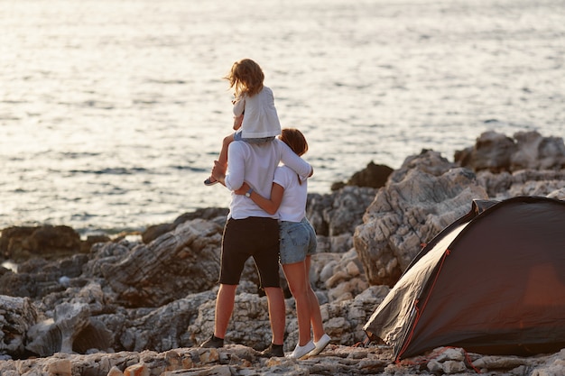 Back view of happy parents with little daughter, sitting on neck.