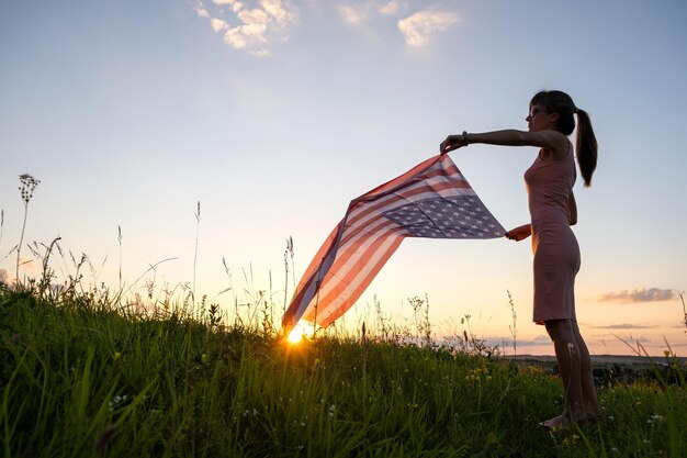 Vista posteriore di una donna felice con la bandiera nazionale degli stati uniti in piedi all'aperto al tramonto donna positiva che celebra il giorno dell'indipendenza degli stati uniti giornata internazionale del concetto di democrazia