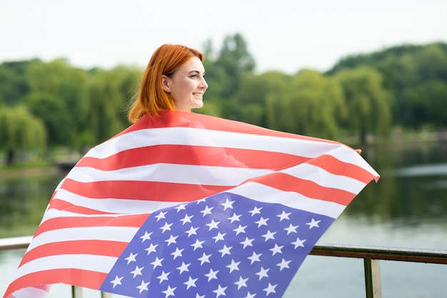 Back view of happy young woman with USA national flag on her shoulders.