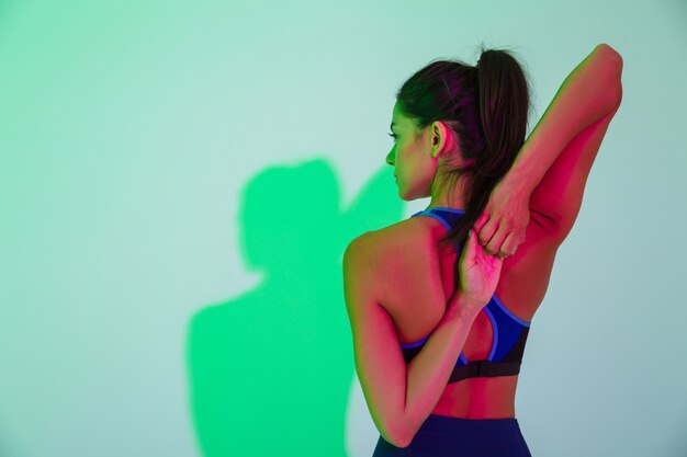 L'immagine della vista posteriore della giovane donna sportiva in posa isolata con luci flash a led fa esercizio di stretching per le braccia.