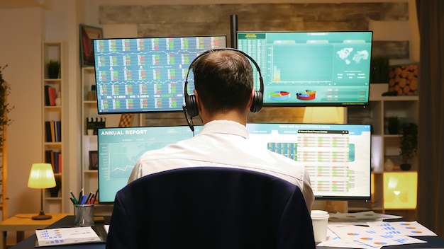 Back view of investor trading stocks online from home office. Businessman with headphones.