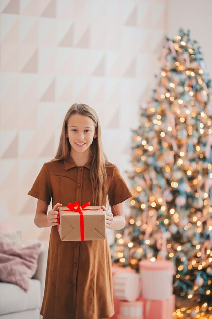 Back view of kid holds a gift box near the christmas tree indoors