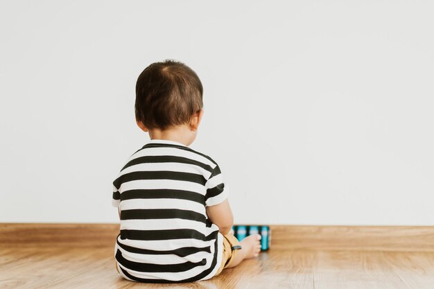 Photo back view of little baby boy sitting alone and watching smartphone