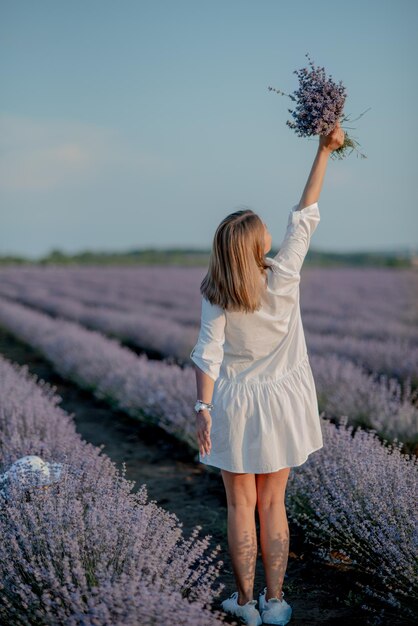 Back view of lovely lady wearing waving white dress hat\
charming young woman in blooming lavender fields lavender essential\
oil with fresh lavender flowers lavendula oleum