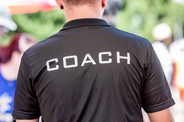 Back view of a male coach wearing black coach shirt with the
white word coach printed on back