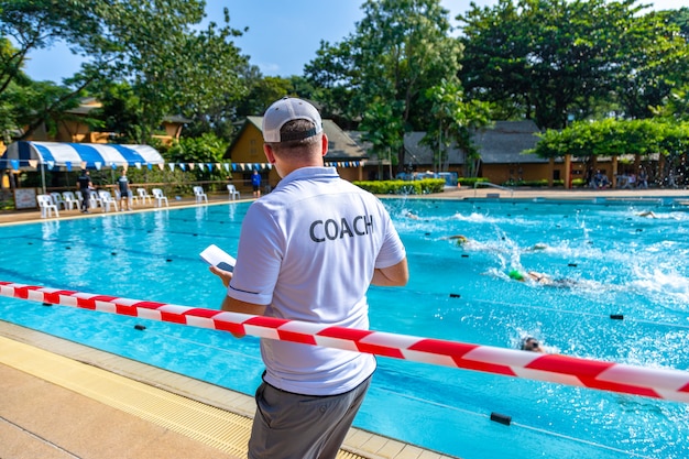 Back view of a male coach in white COACH shirt watching his swimmers racing