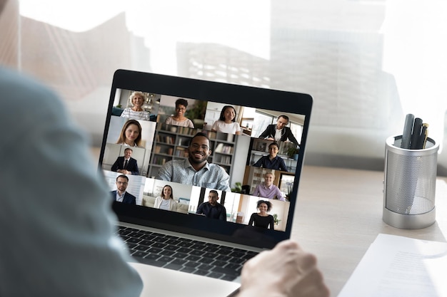 Back view of male employee have online video call on laptop with diverse multiethnic colleagues man worker involved in webcam conference or virtual event on computer with multiracial businesspeople
