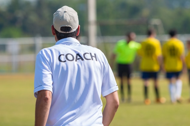 Vista posteriore del allenatore di calcio maschile in camicia di coach bianco in un campo sportivo all'aperto