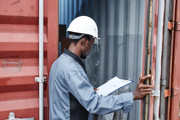 Back view of male worker wearing hardhat while checking\
containers at shipping dock copy space