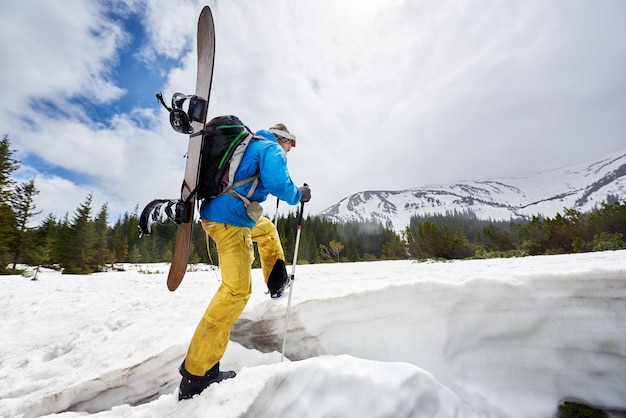 Back view of man carrying snowboard on his back on challenging snowy route for offpiste snowboarding riding Copy space