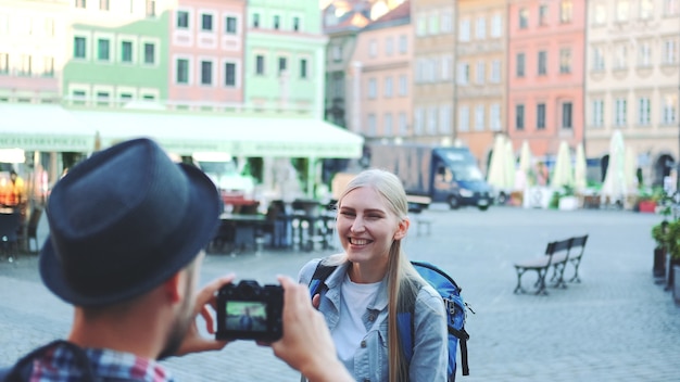 Вид сзади мужчины, фотографирующего туристку на фоне рыночной площади города